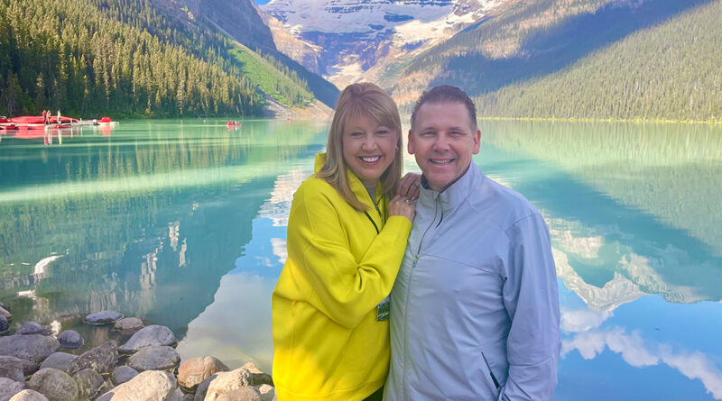 Vickie and Jeff Carr smile during a vacation in front of the water and mountains