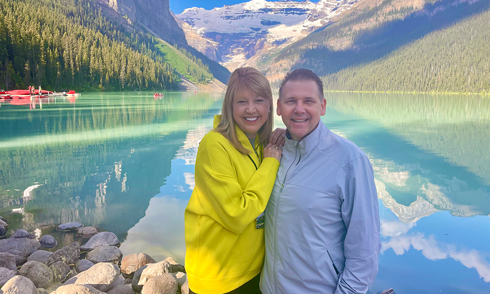 Vickie and Jeff Carr smile during a vacation in front of the water and mountains